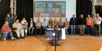 Das Bild zeigt die Teilnehmer*innen des Netzwerktreffens in der Färberei in Wuppertal und zugeschaltet über Zoom auf einer Leinwand. Foto KSL Düsseldorf